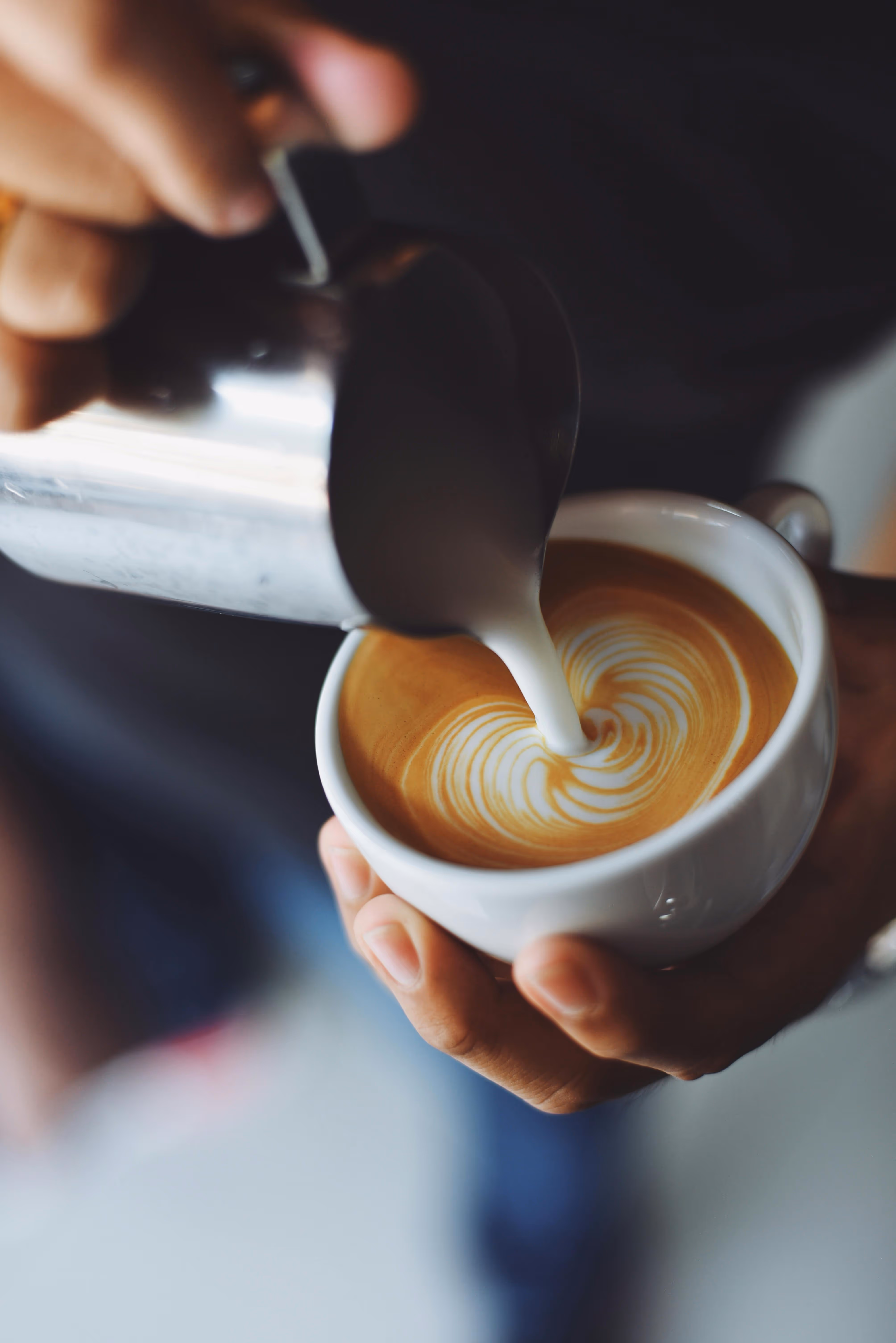 A skilled barista pouring steamed milk into a cup of expertly crafted latte, creating a swirling heart design. This image embodies the passion for coffee culture and craftsmanship, perfect for any café or coffee enthusiast's website.