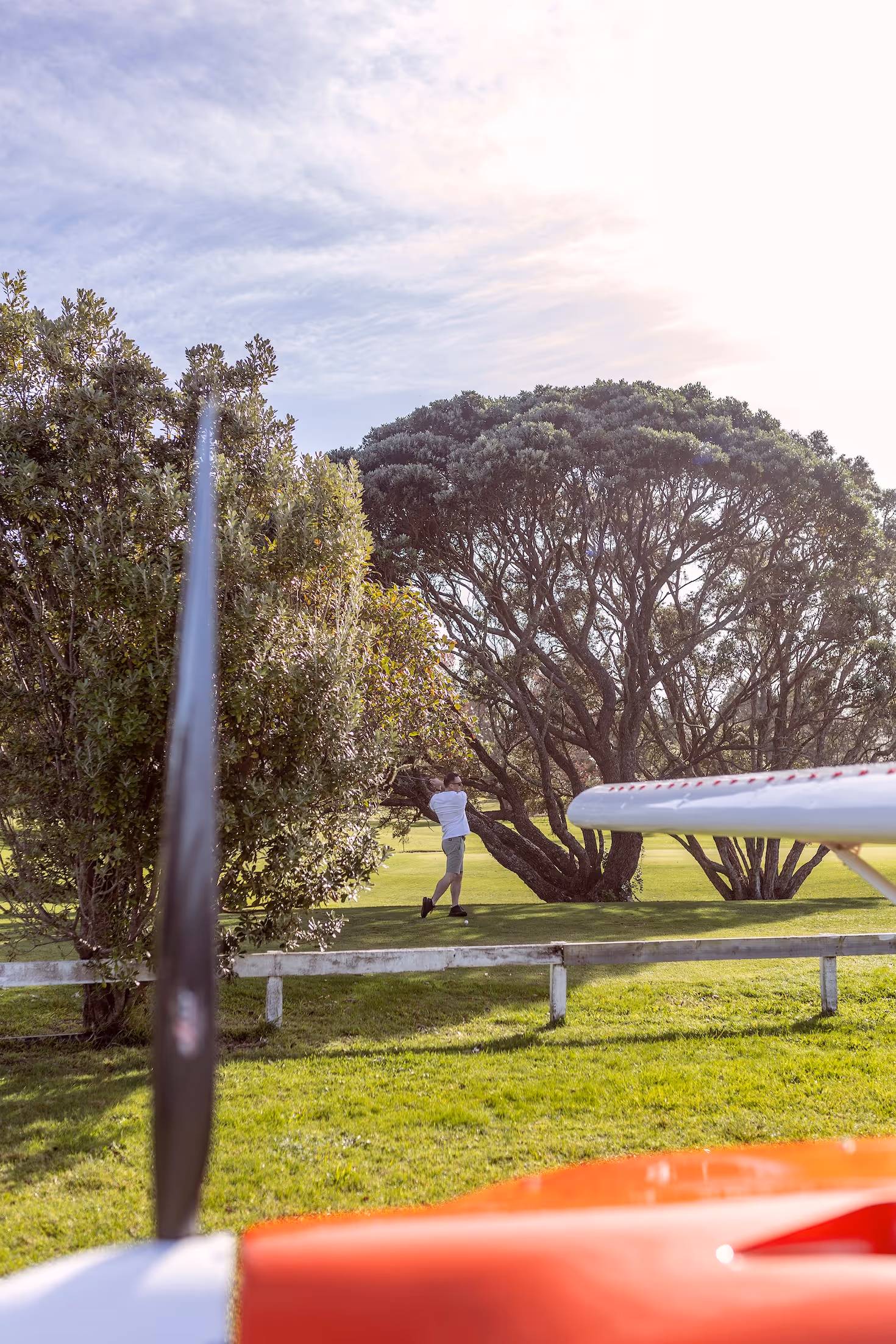 Aviation enthusiast enjoying leisure time at Te Kowhai Airpark, framed by lush greenery and a private aircraft in the foreground. The setting highlights the unique lifestyle of living among aviation in New Zealand's first purpose-built aviation community.