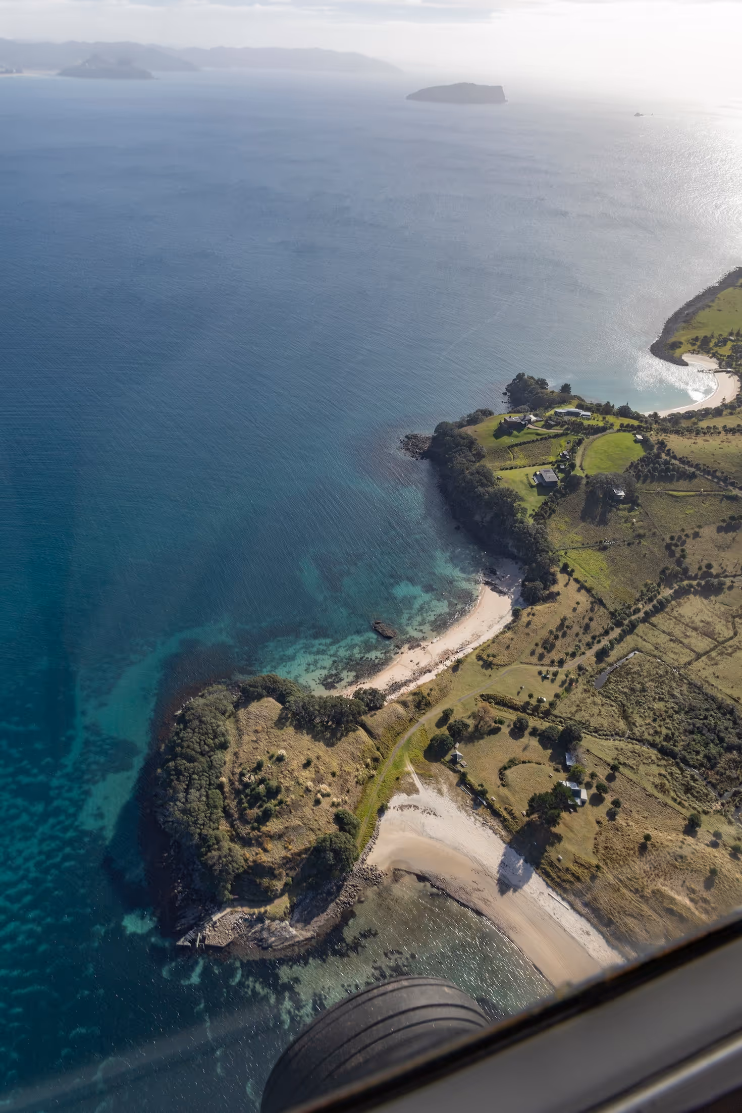 Aerial view of a scenic coastline in New Zealand, showcasing tranquil turquoise waters, golden sandy beaches, and lush green properties, embodying the unique lifestyle around Te Kowhai Airpark and its aviation community in the Waikato region.