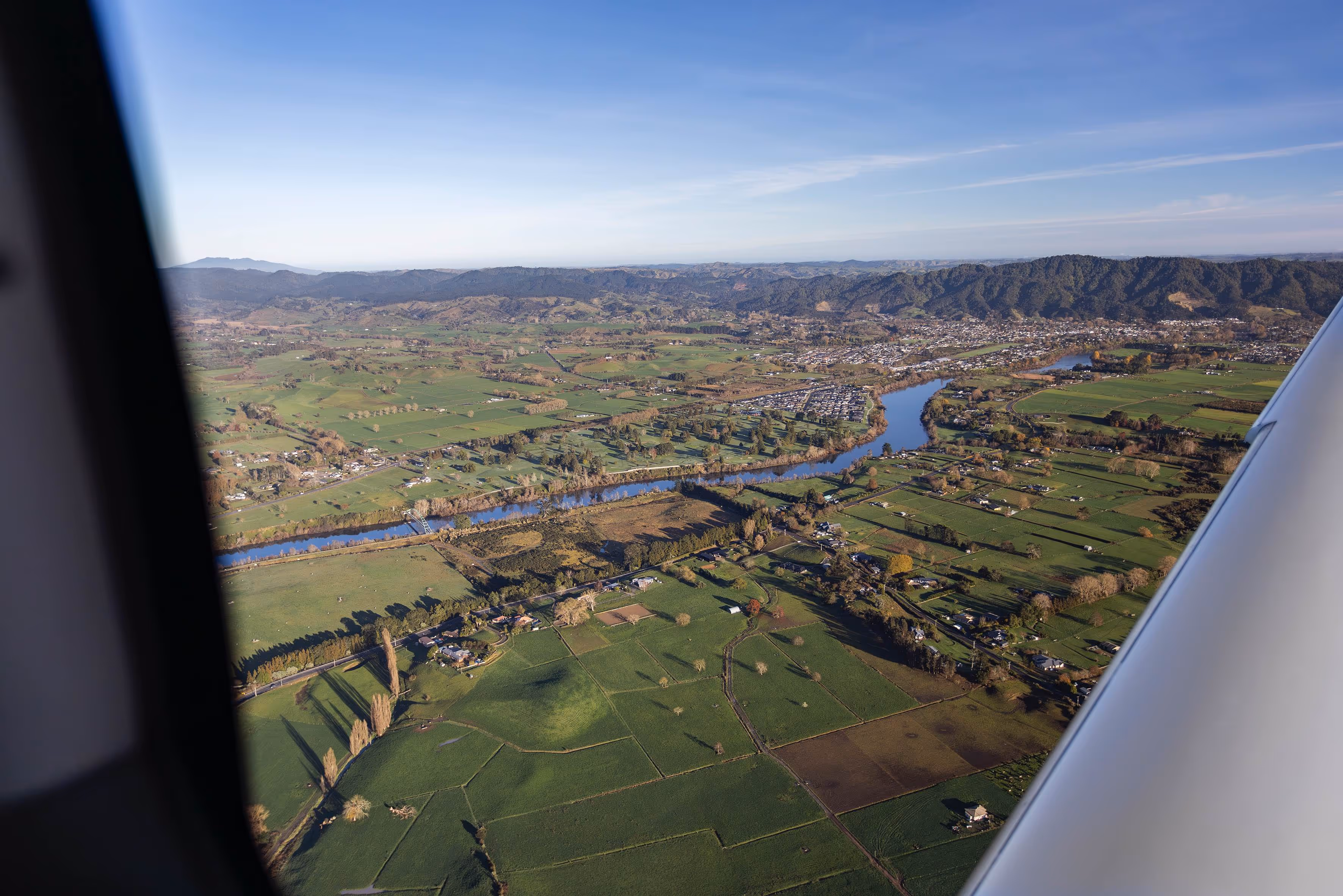 Aerial view of the picturesque Waikato landscape near Te Kowhai Airpark, showcasing lush greenery, flowing rivers, and the integration of residential areas within the scenic countryside, highlighting the unique aviation community lifestyle.