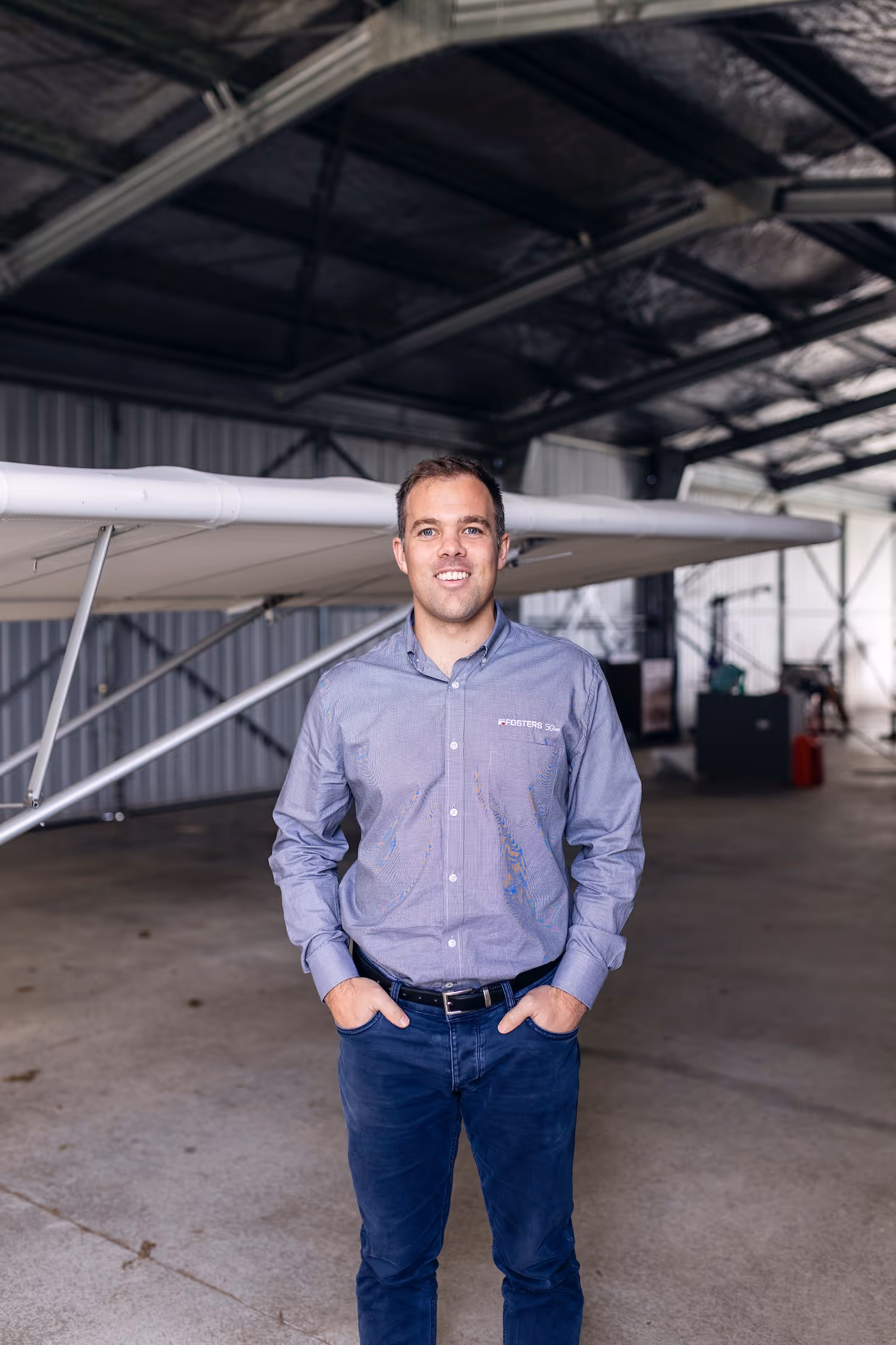 A man stands confidently in a hangar at Te Kowhai Airpark, New Zealand, with a light aircraft in the background. The image showcases the unique blend of aviation and lifestyle in this residential aviation community.