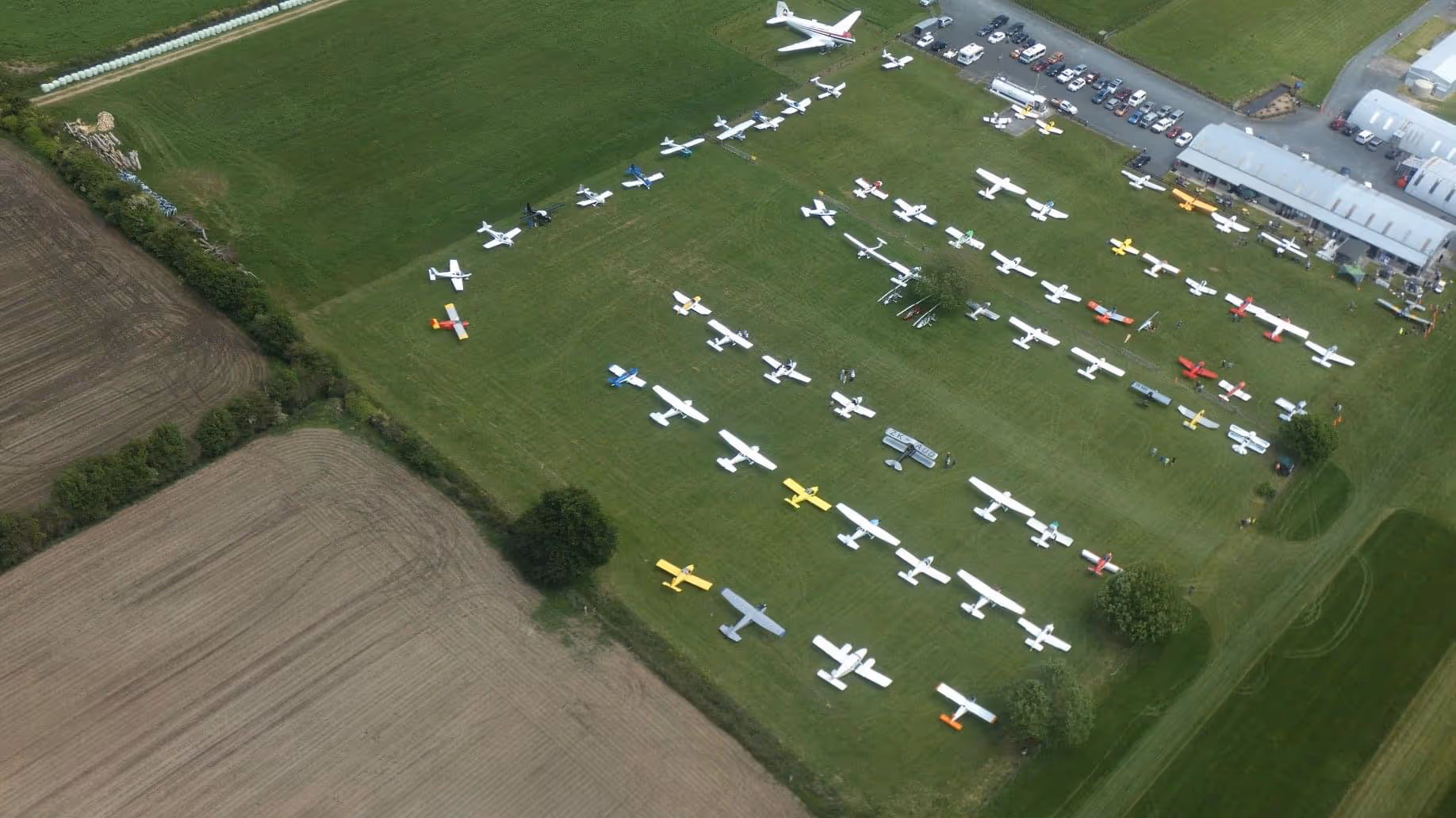 Aerial view of Te Kowhai Airpark showcasing a variety of aircraft parked on a green field, surrounded by lush landscapes. The image highlights the vibrant aviation community, featuring residential hangars and easy access to the airfield in the Waikato region of New Zealand.