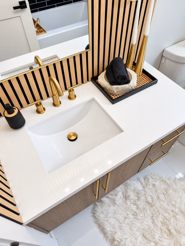 Mukilteo, WA — Close view of the light vanity counter, warm metal faucet, dark cabinet fronts, and wood-slat wall.