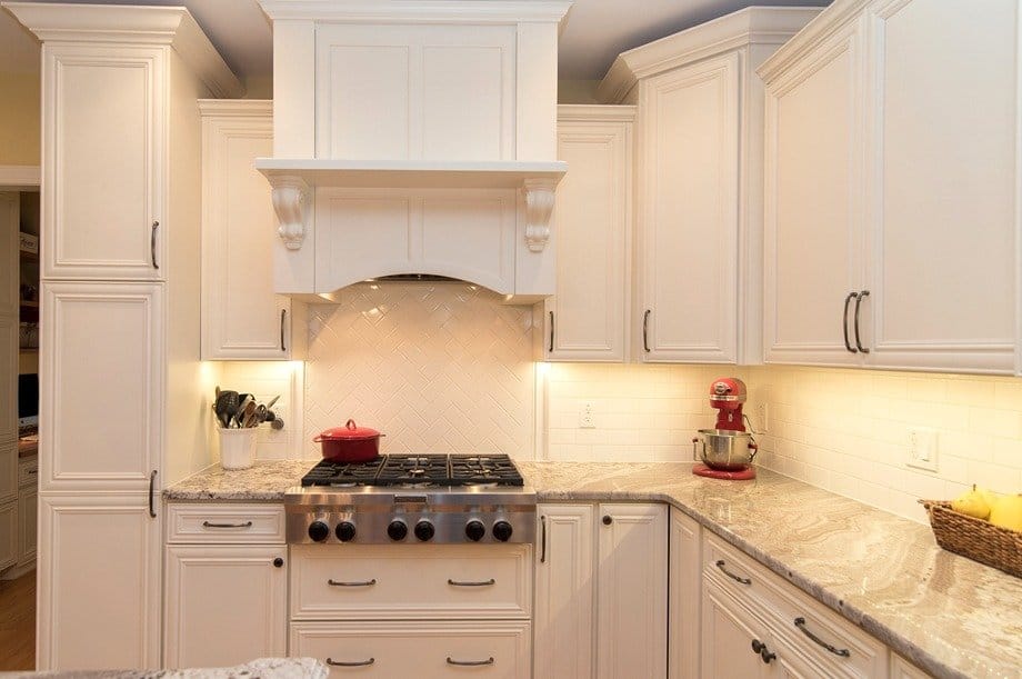 White kitchen cabinetry with under-cabinet lighting, a large range hood, and light countertops.