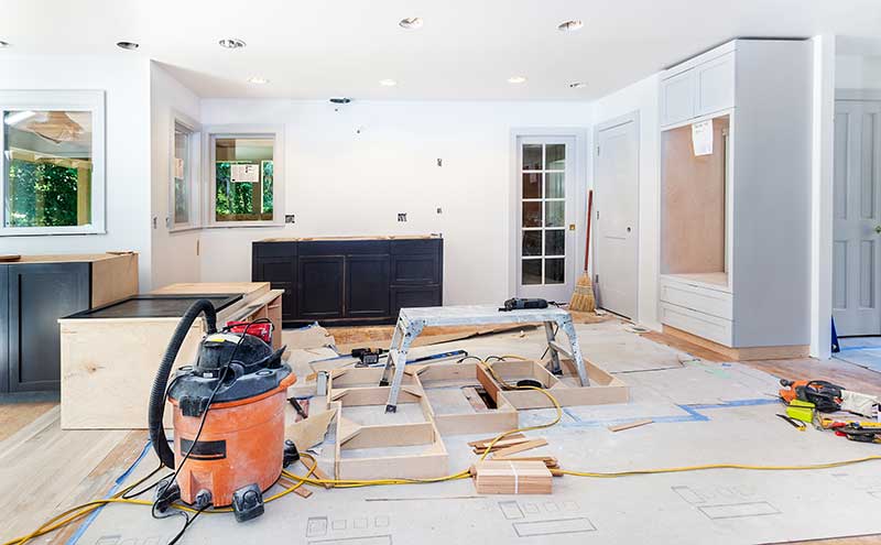 Kitchen under renovation with tools, materials, exposed flooring, and partially installed cabinetry.