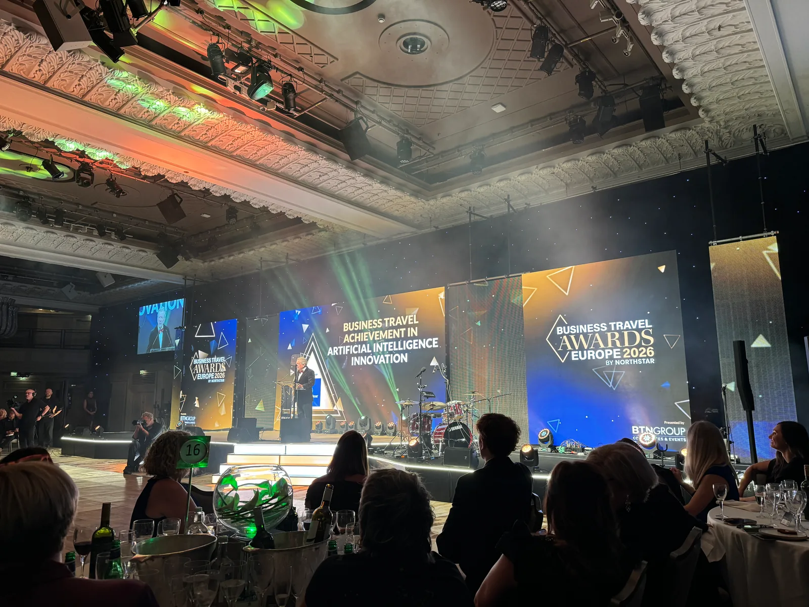 Business Travel Achievement in Artificial Intelligence Innovation on the stage screen, someone at the lectern below