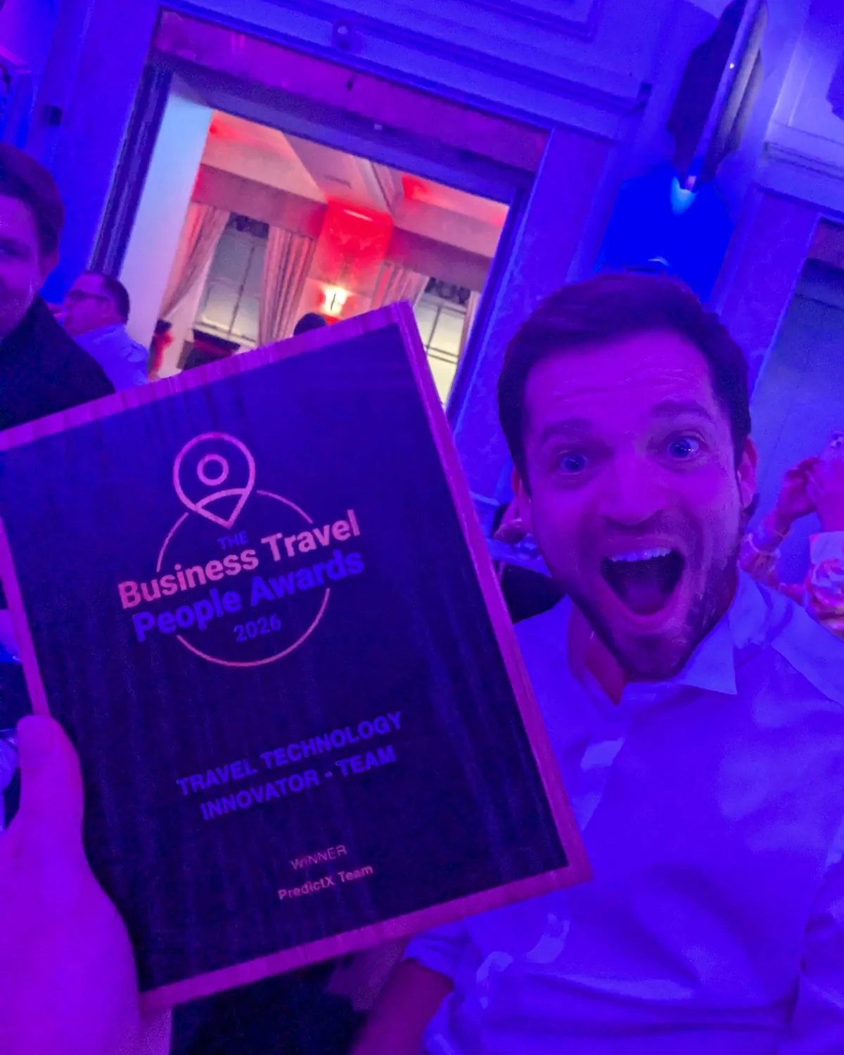 A man shouts with joy under purple light beside the plaque, which names the PredictX Team