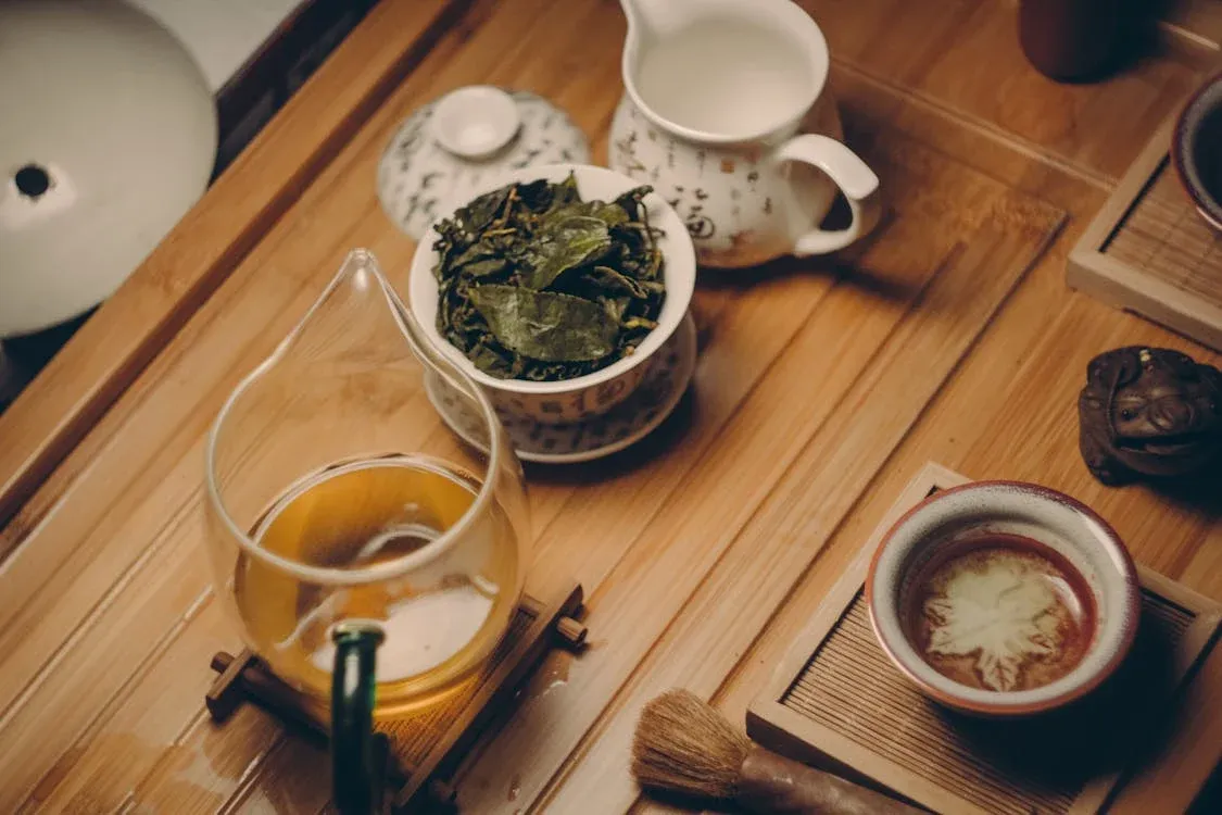 Traditional Chinese tea set on a wooden tray, including a glass pitcher with tea, a bowl with tea leaves, a small cup, a milk pitcher, and a tea brush.