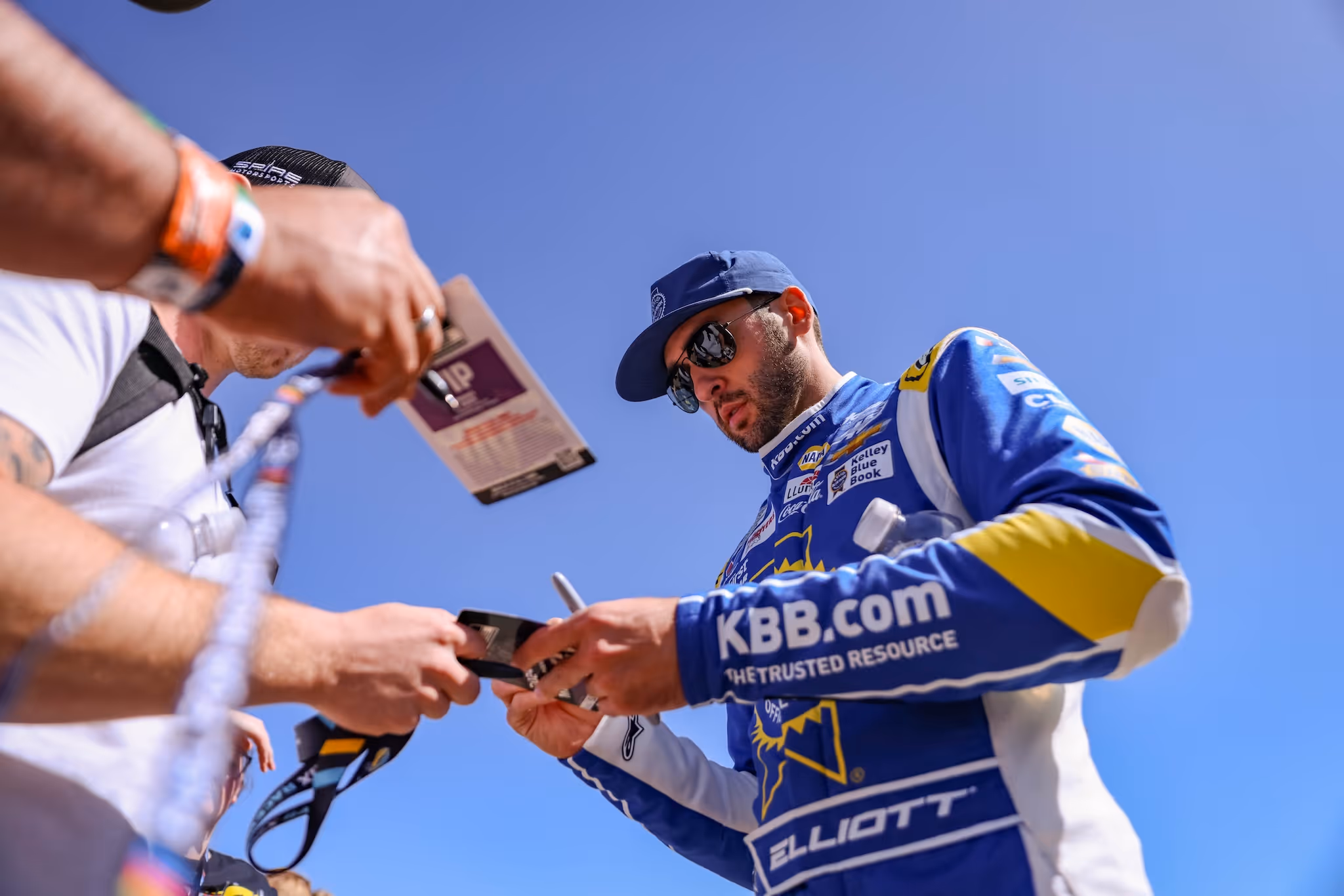 Race car driver Chase Elliott in blue KBB.com racing suit signing autographs for fans.