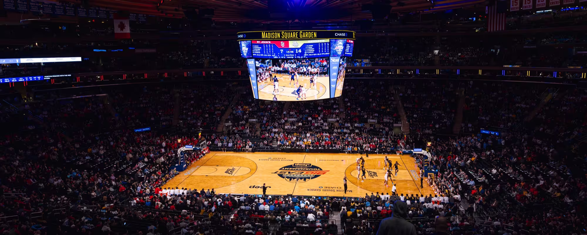Wide view of a basketball game in progress at Madison Square Garden with a large crowd and scoreboard overhead.