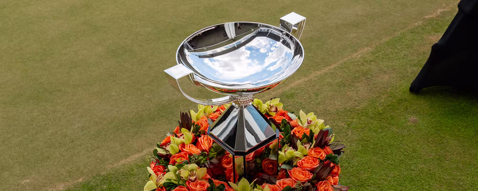 Silver trophy cup surrounded by a wreath of orange and green flowers on green grass.