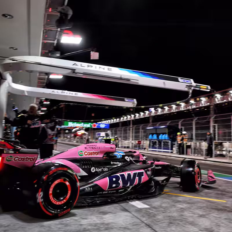 Pink and black BWT Formula 1 car in a night-time pit lane with Alpine branded equipment and crew around.
