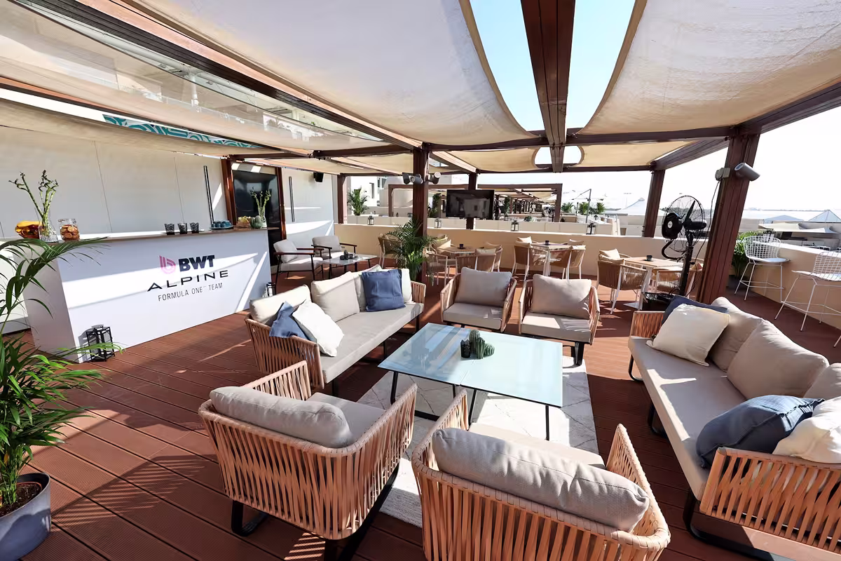 Outdoor seating area with cushioned sofas and chairs under a canopy, featuring a BWT Alpine Formula One team bar counter.
