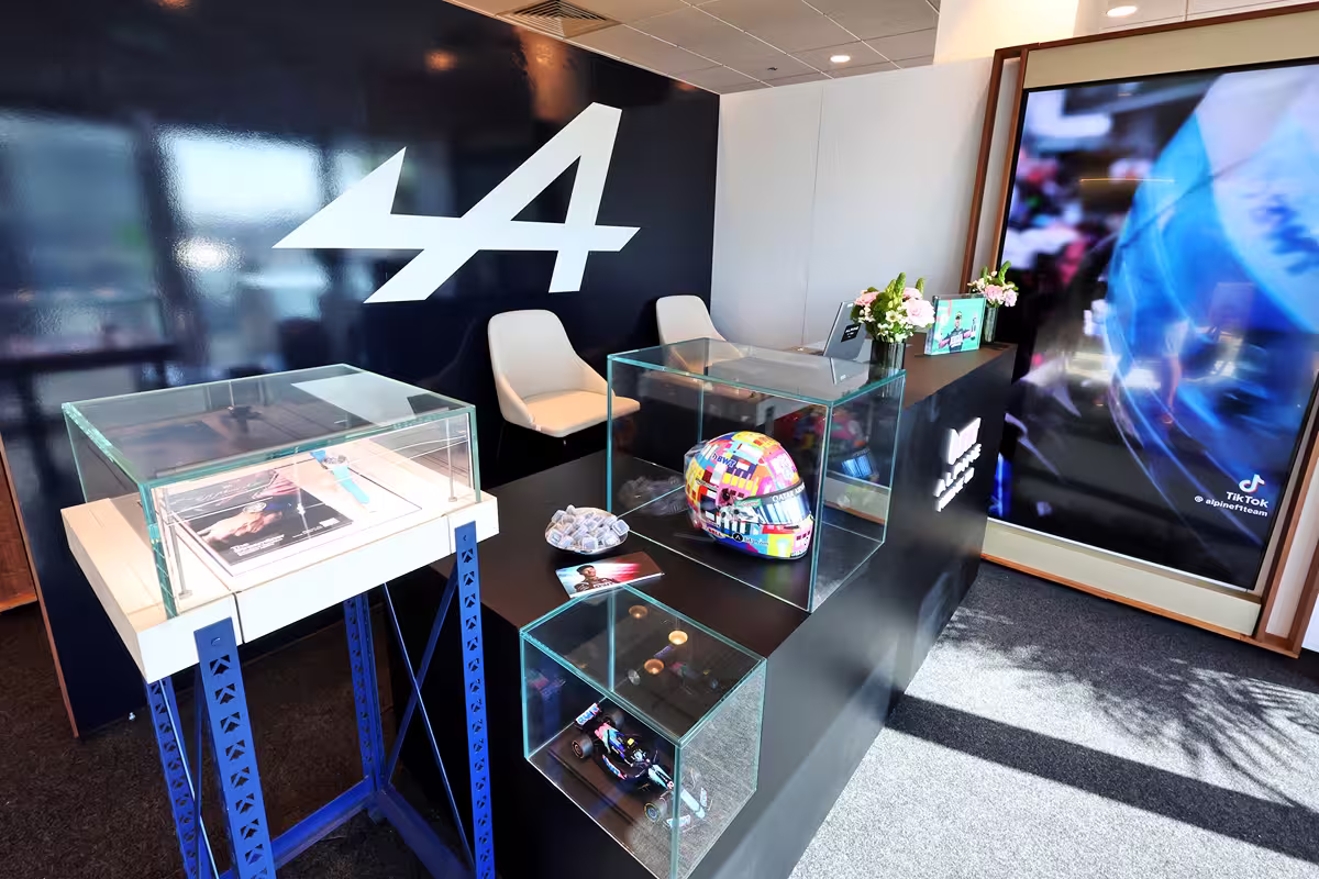 Display area with Alpine F1 Team logo, featuring a colorful racing helmet, miniature car model, and promotional materials under glass cases.