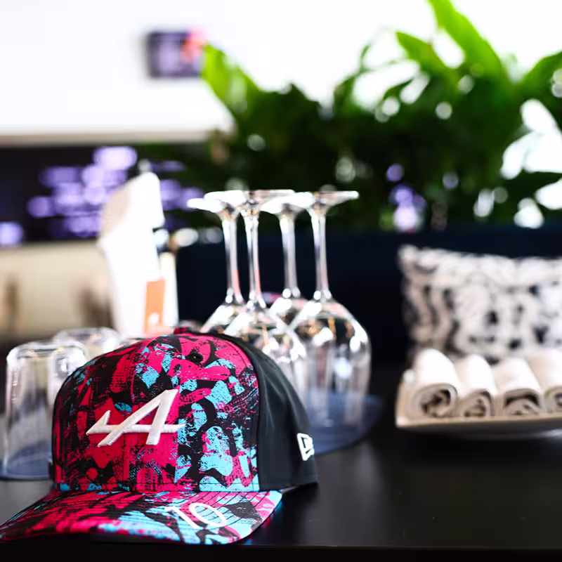 Colorful baseball cap with an 'A' logo on a table next to inverted wine glasses and a vase of flowers.