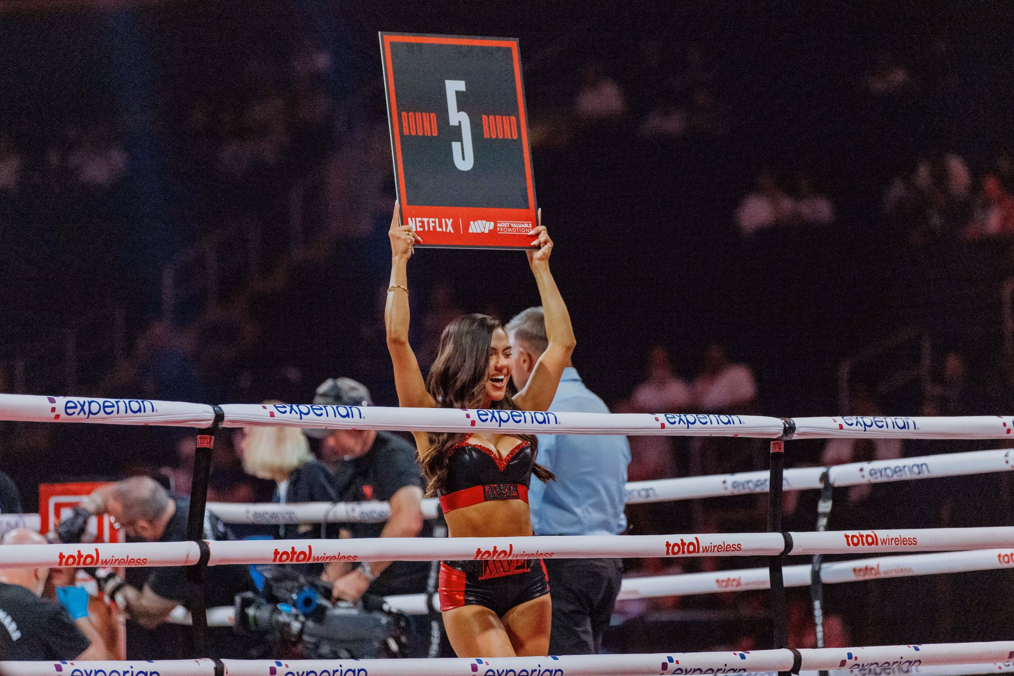 Ring girl inside boxing ring holding up a sign indicating round 5 during a boxing match.