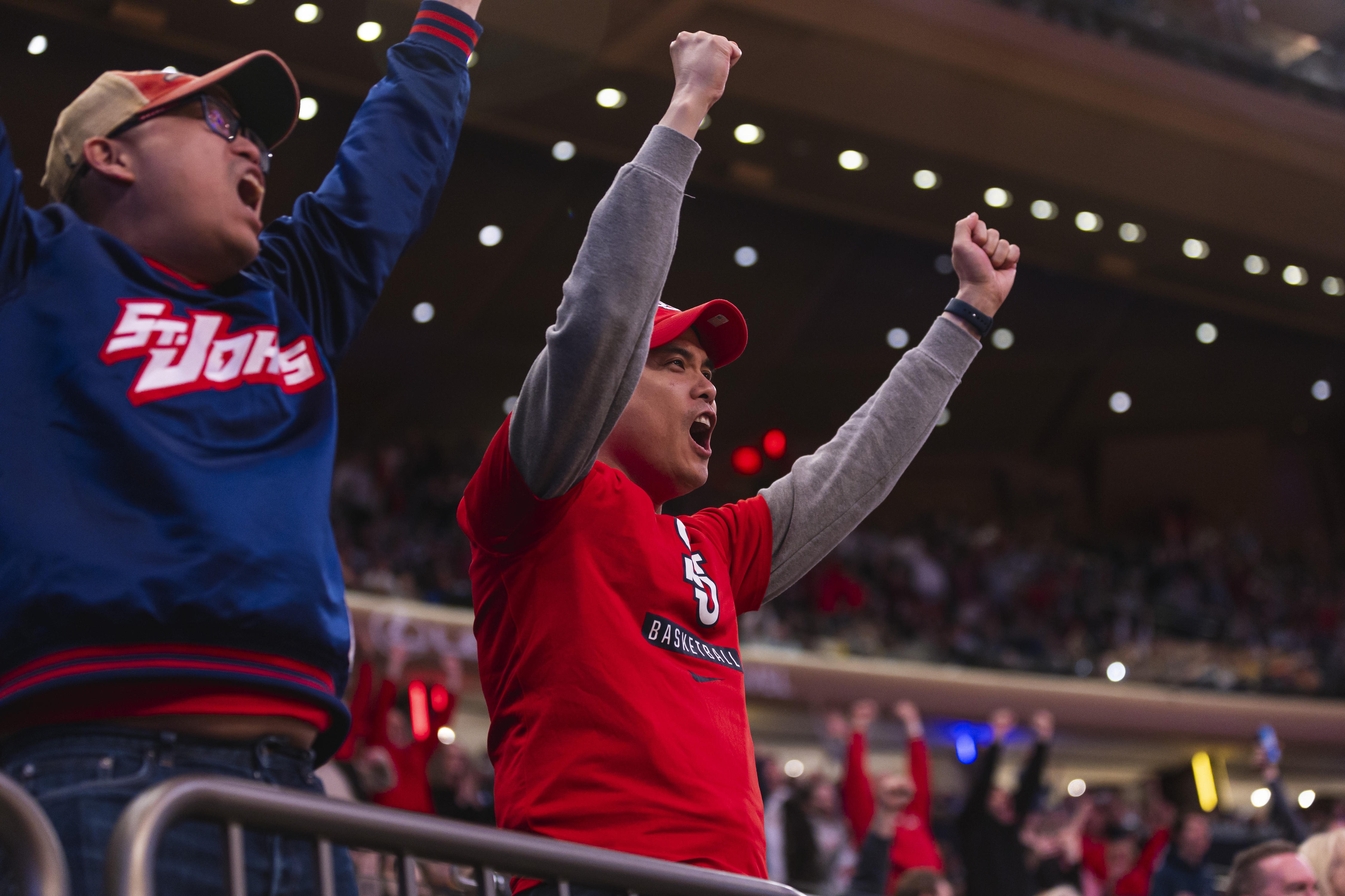Two enthusiastic fans cheering with raised fists at a basketball game in an indoor stadium.