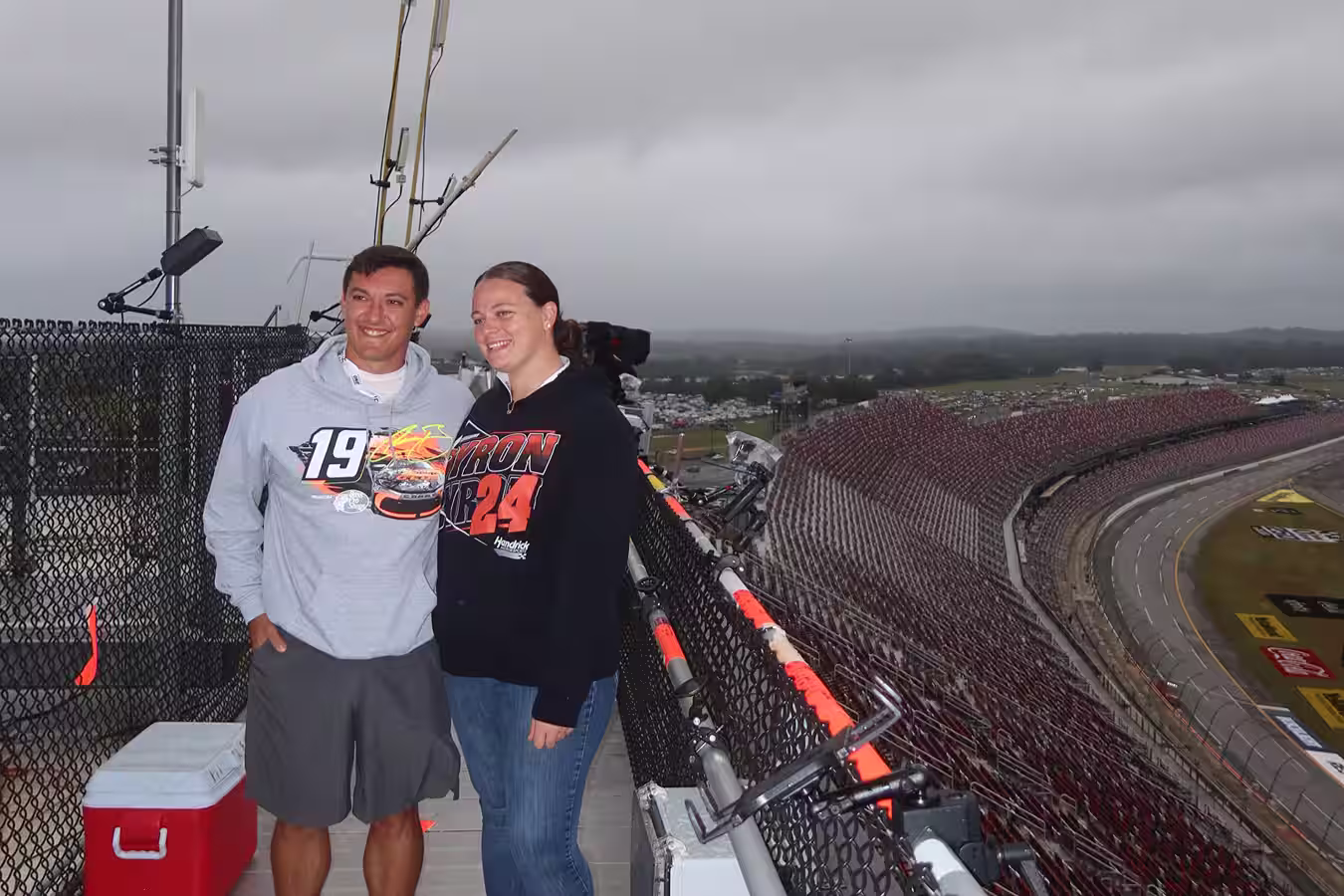 A young fan in a Pennzoil racing shirt posing for a photo taken by a man wearing an Arson 5 t-shirt at a racetrack viewpoint.