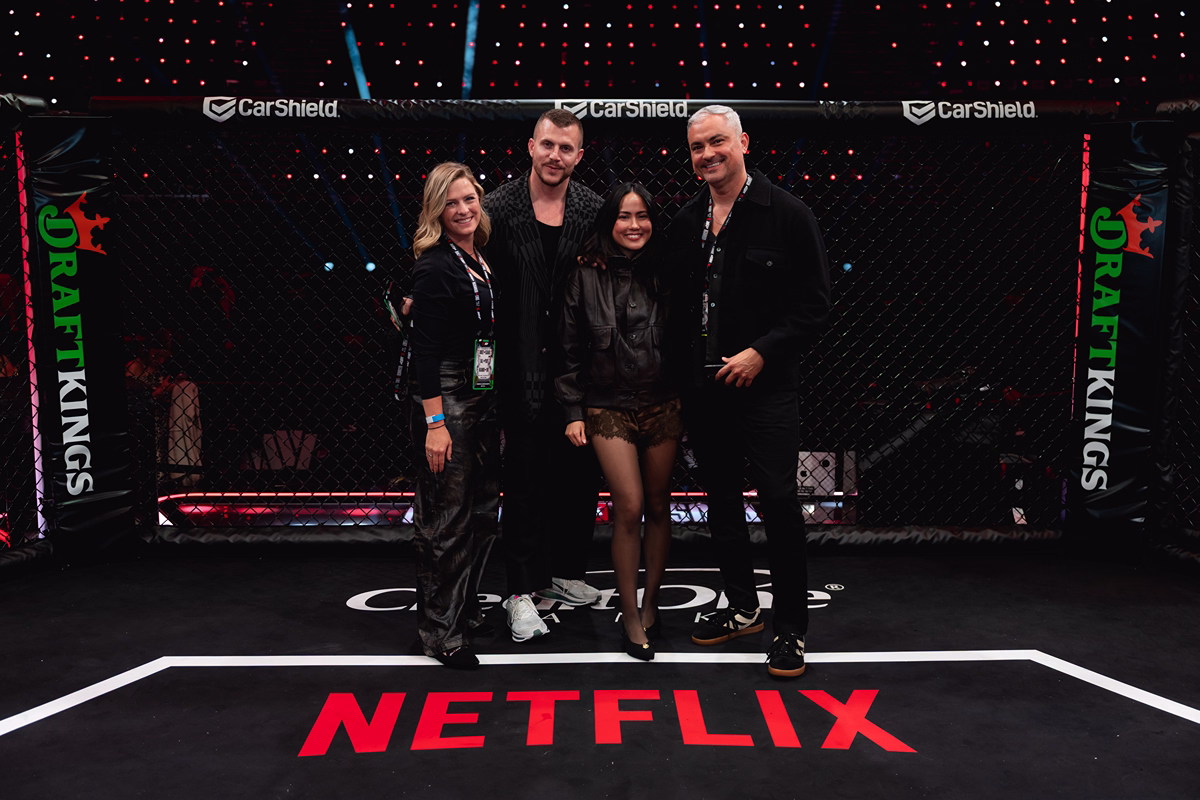 Four people standing together inside an MMA fighting cage with DraftKings logos on the cage and a large Netflix logo on the floor beneath them.