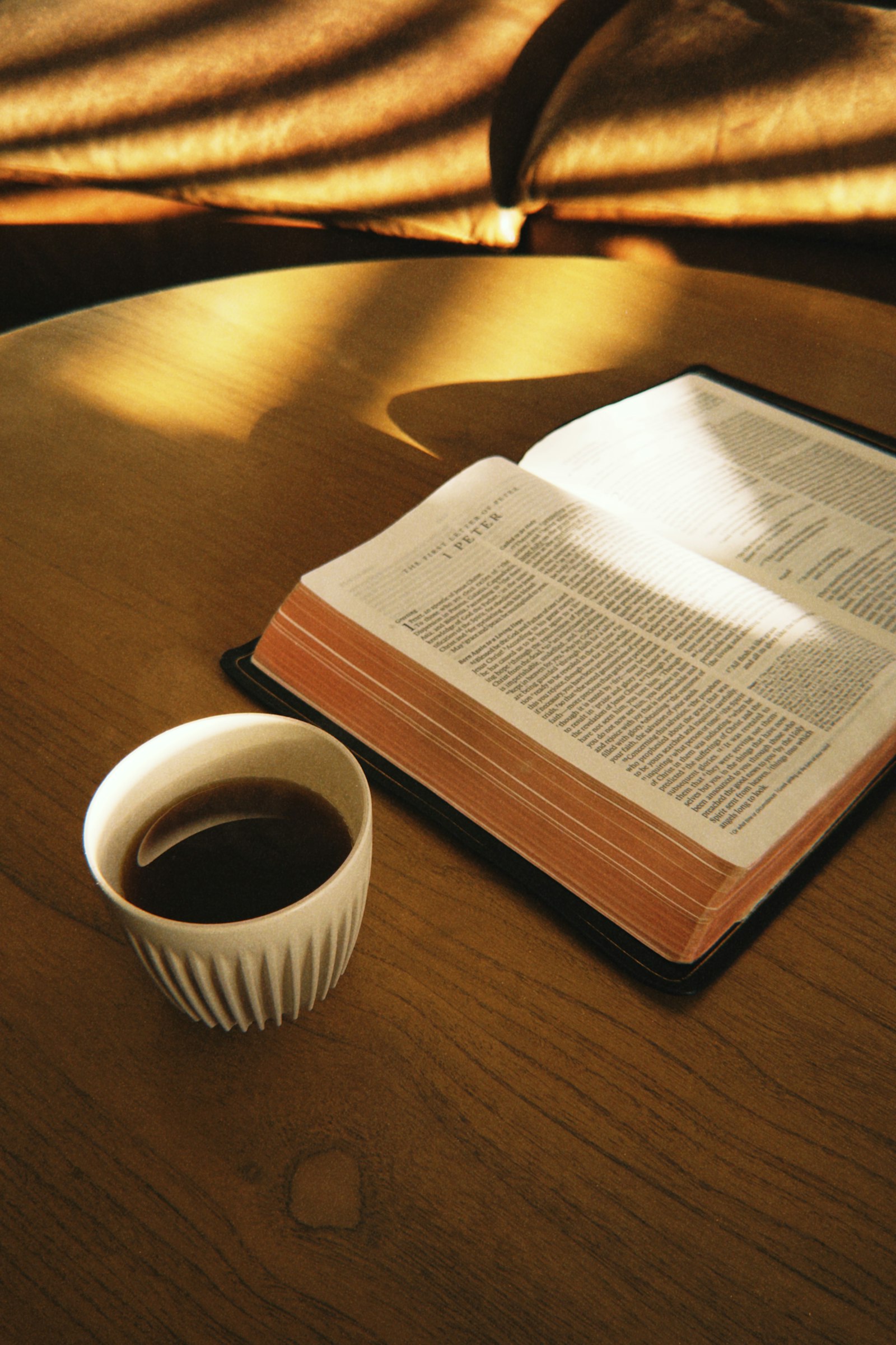 An open Bible and a cup of coffee on a sunlit wooden table (temporary photo)