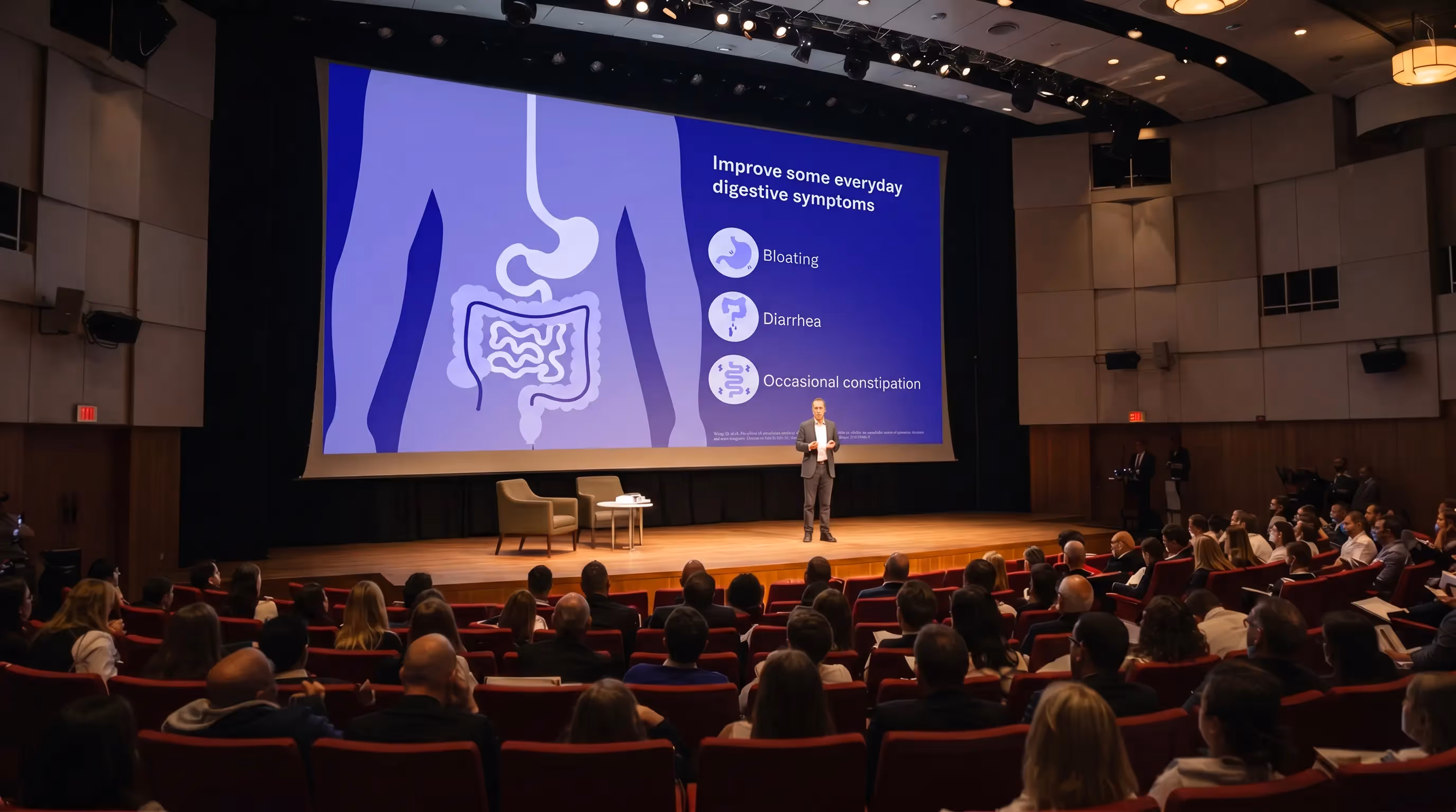 Conference presentation showing digestive system infographic highlighting symptoms like bloating diarrhea and constipation