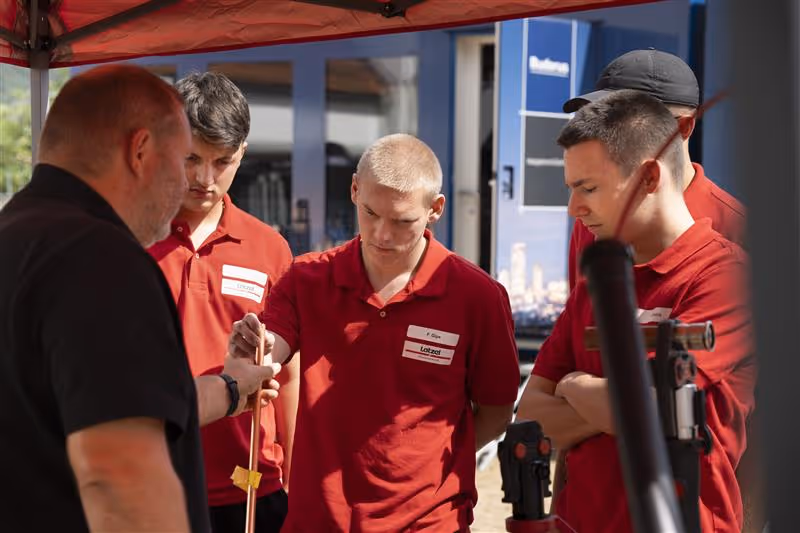 Ausbildungsleiter zeigt Latzel Azubis etwas auf dem Handy.