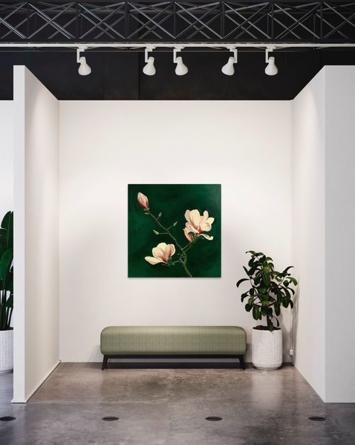Minimalistic room with a bench and houseplant with Magnolia painting hanged on the wall. Painting has a branch of magnolia flowers against dark green background.