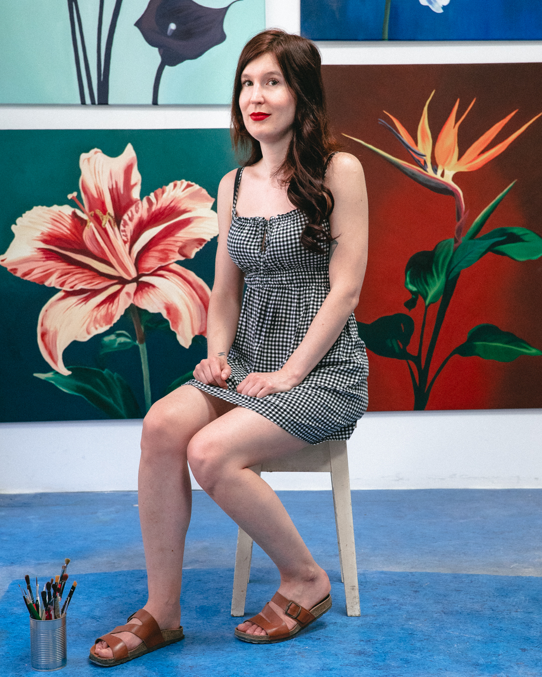 A picture of artist Zuzanna Rajewska sitting on a chair with her paintings in the background