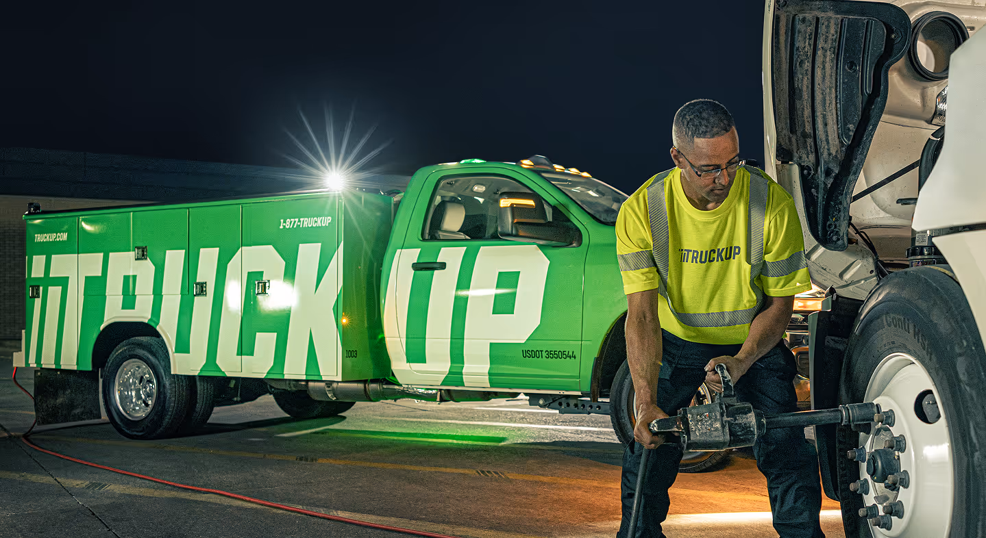 TruckUp operator using a power wrench to work on a large truck tire at night with a green iTruckUP service truck in the background.