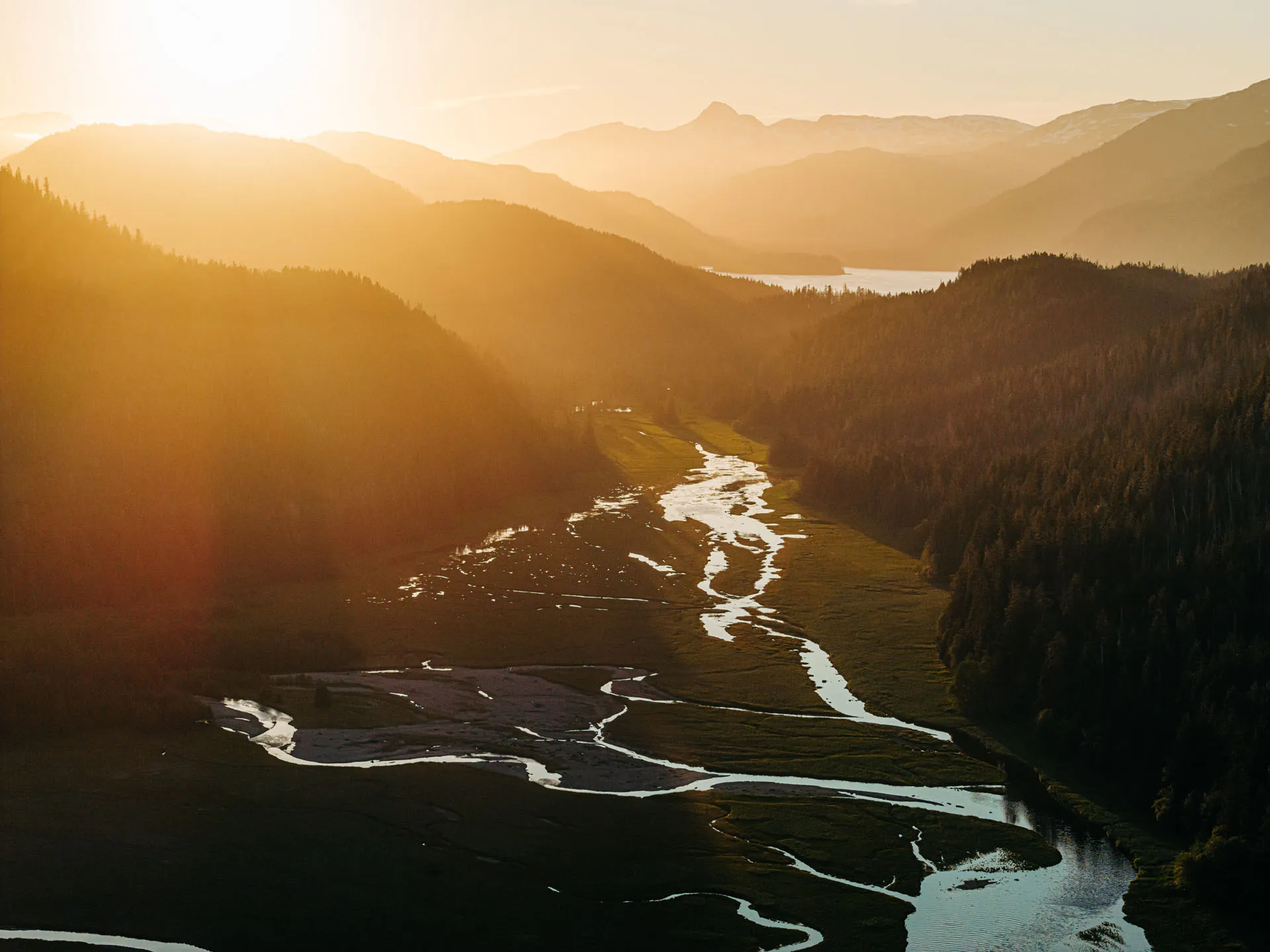Golden evening light over a braided river estuary and forested mountains near Sitka
