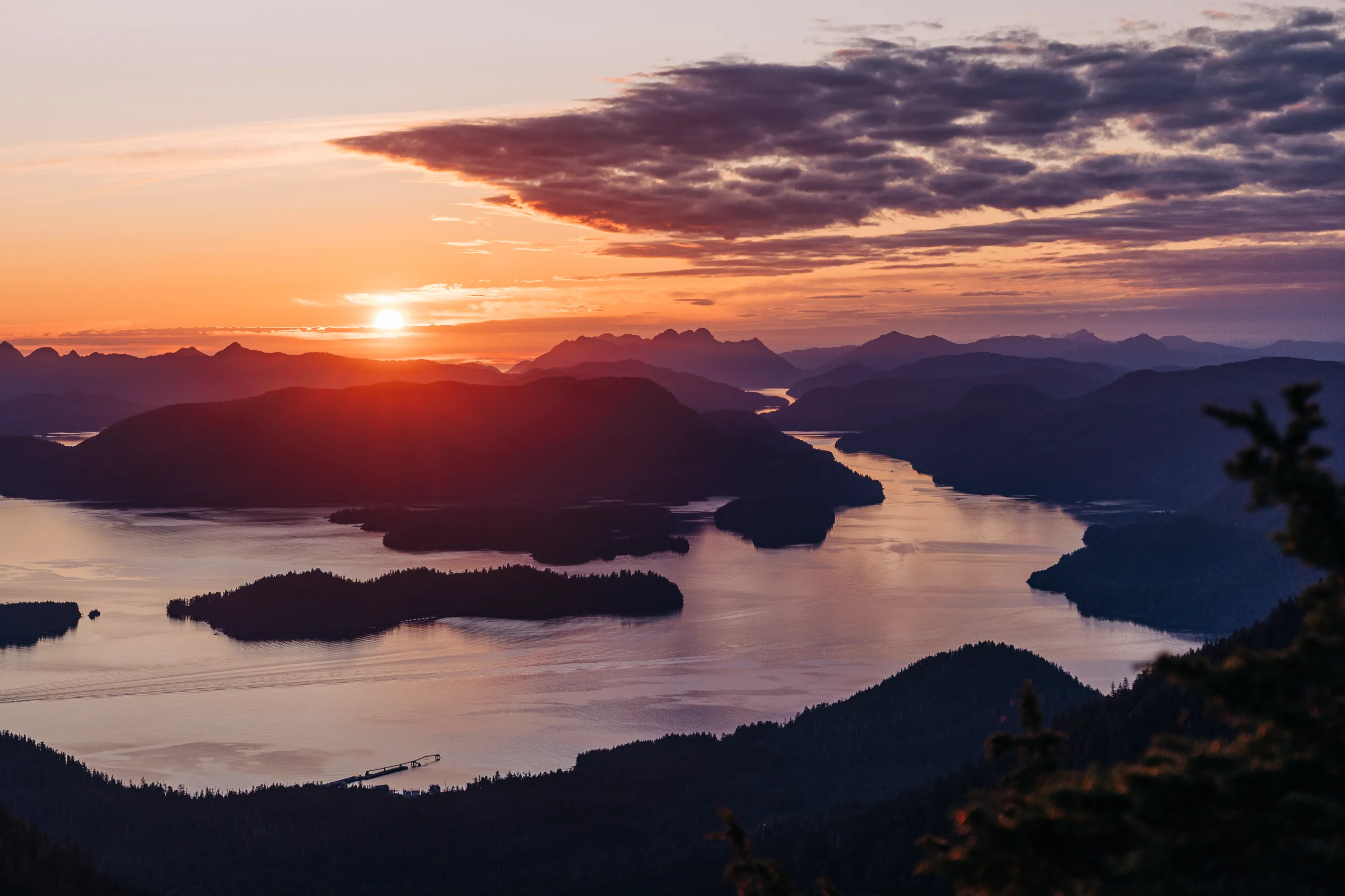 Sunset over a mountainous landscape with a winding river or inlet reflecting the orange and purple sky.