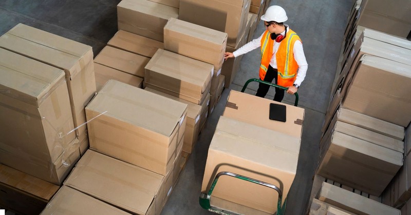 a warehouse worker picking up a bunch of boxes with a trolley