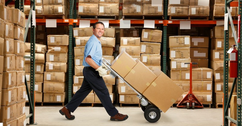 a warehouse employee pushing a cart with a bunch of boxes