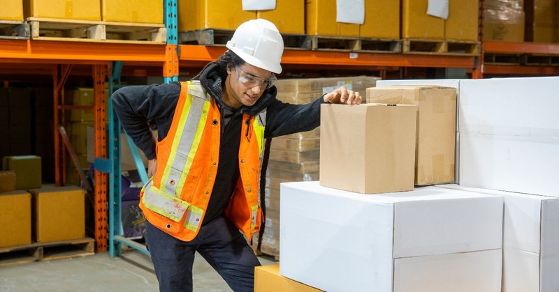 a warehouse worker experiencing back pain while handling boxes