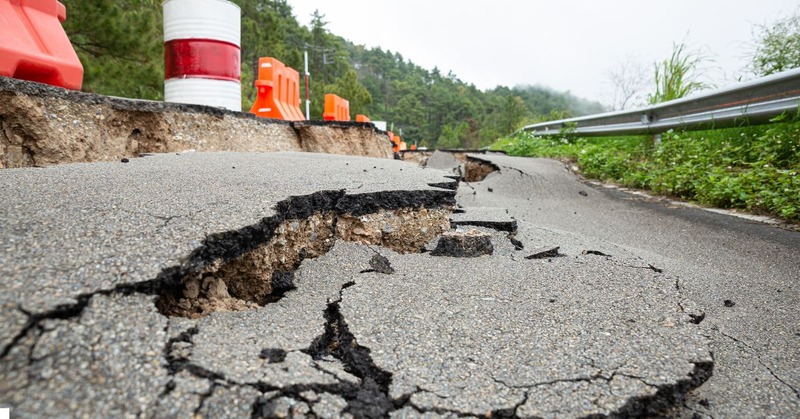 a damaged road with large cracks and pieces of asphalt that have broken apart