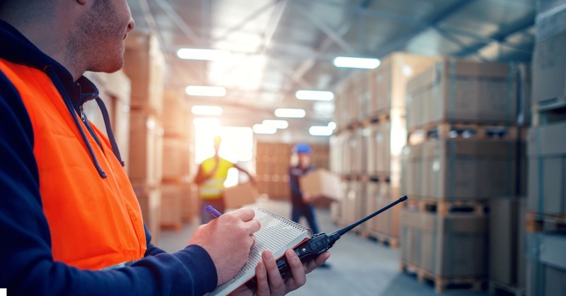 a warehouse worker holding a list and walkie-talkie