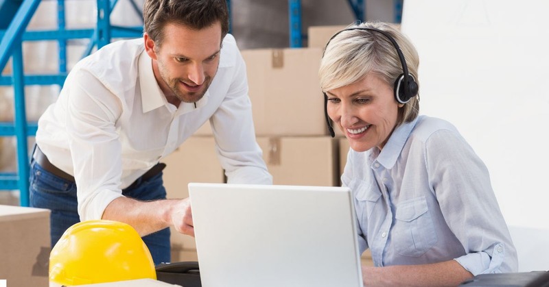 a warehouse worker's working together while looking at the laptop