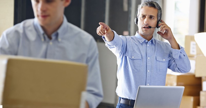 a warehouse worker wearing a headset and talking while pointing at something