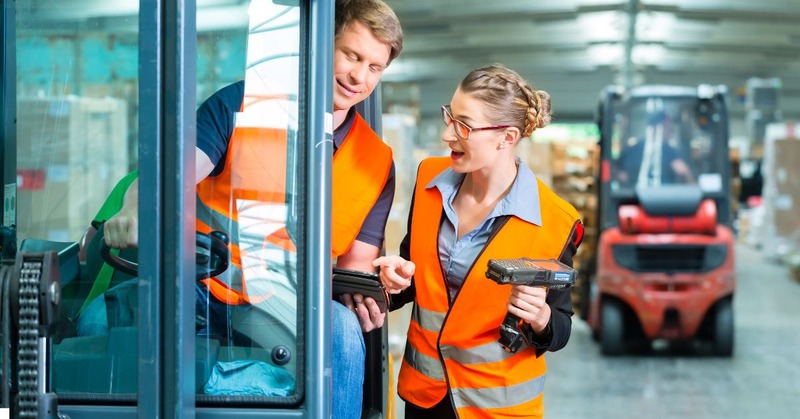 a warehouse worker's talking while holding scanner and driving forklift