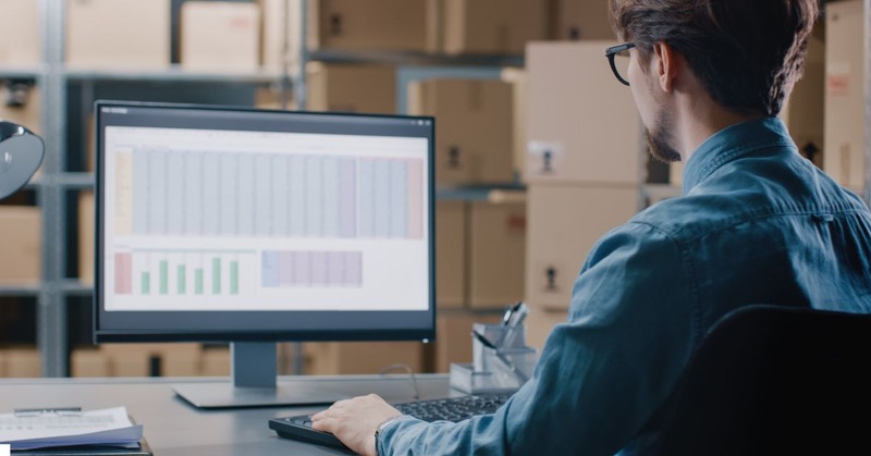 a warehouse employee facing a computer and calculating a report