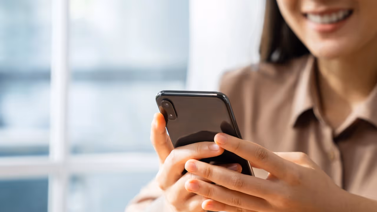 A zoomed in view of a woman smiling looking at her cell phone.