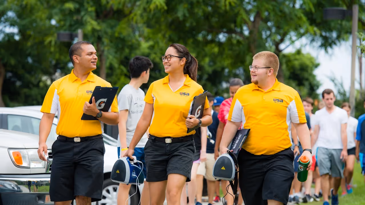 A diverse group of event organizers wearing matching yellow shirts and carrying clipboards while walking together.
