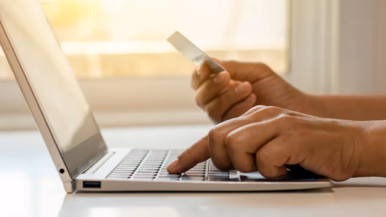 Zoomed in view of a woman's hands on a keyboard typing while holding a credit card.