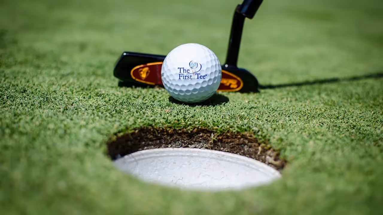 Zoomed in view of a putter about to tap a golf ball into the hole on the green.