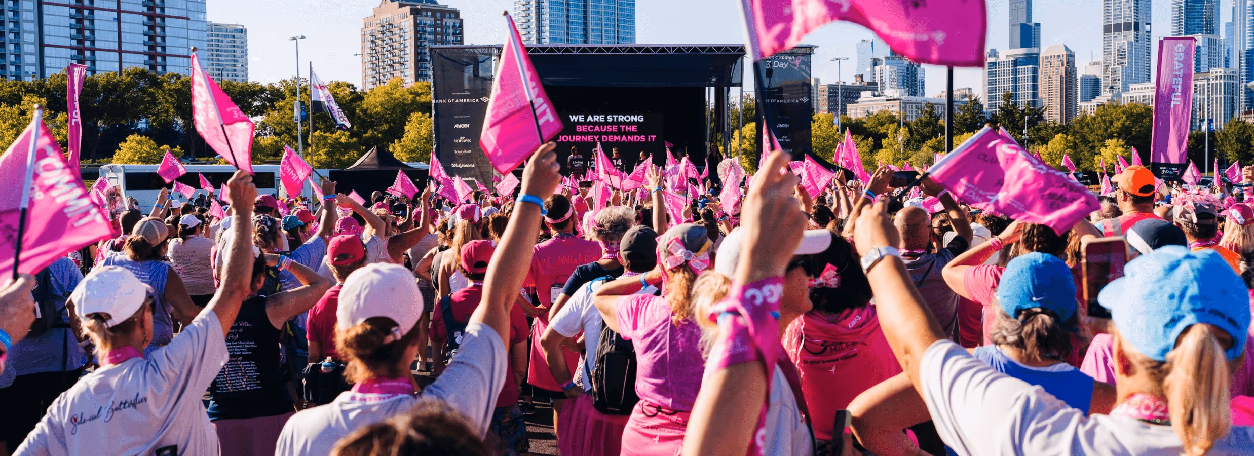 Gathering of people at an outdoor event wearing pink and waving pink flags.