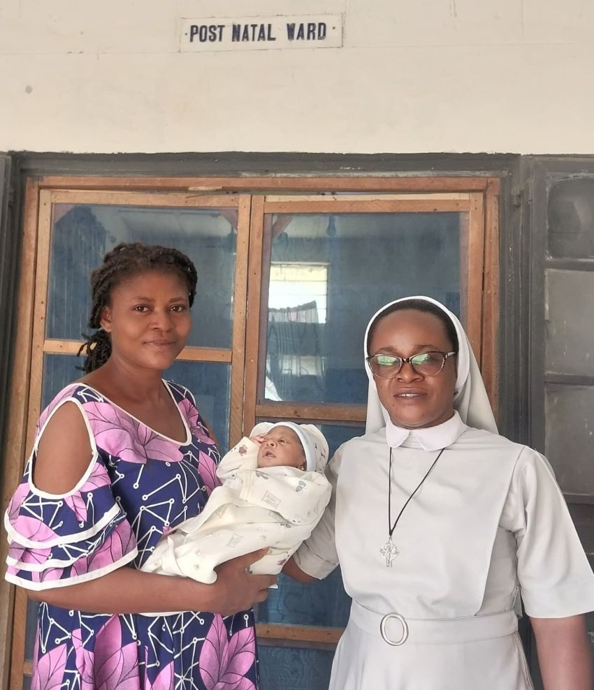 A religious sister and mother with newborn smile in front of the Post Natal Ward of a hospital