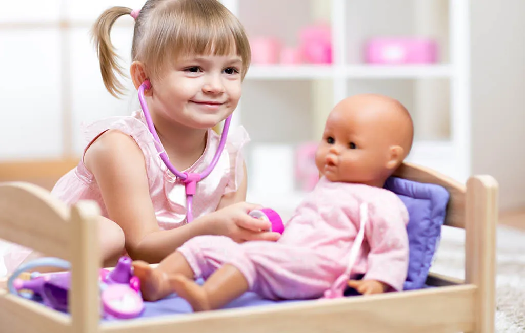 Child playing doctor with a doll toy while the doll lies in the doll’s bed.