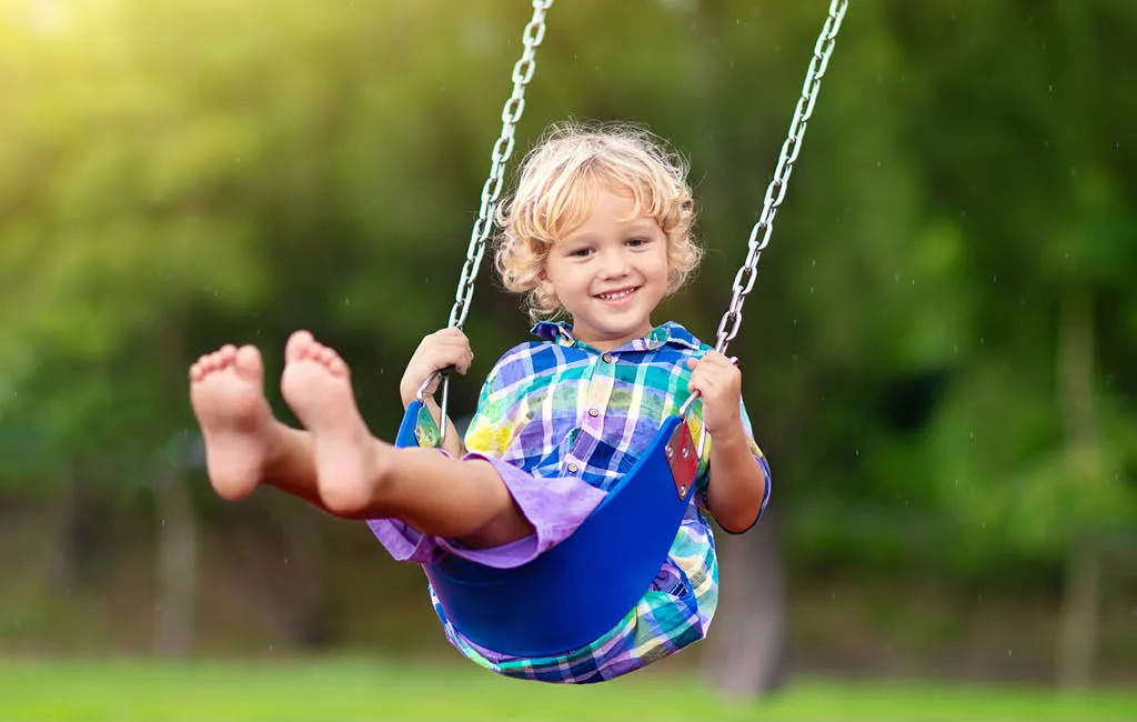 A blond boy swings outdoors.