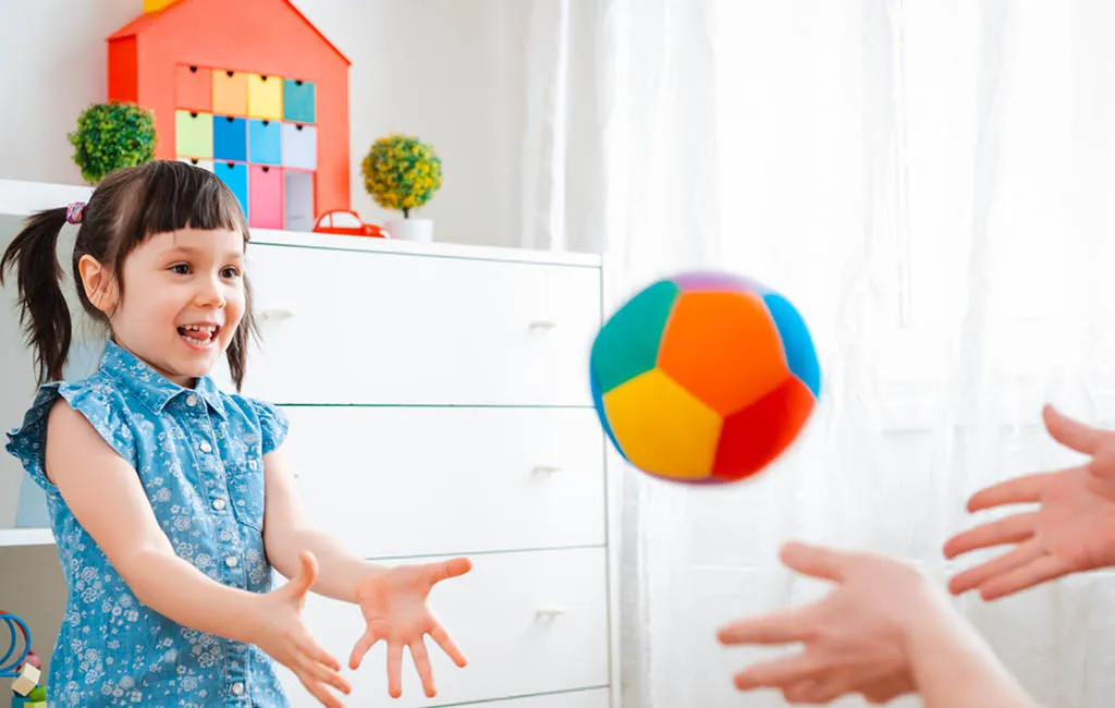 A parent and a preschool child play catch with a ball in a children's room.