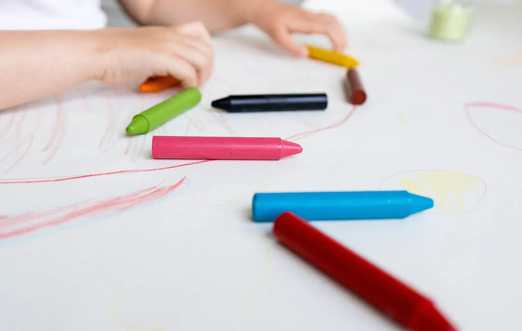 Child drawing with wax crayons on white paper.